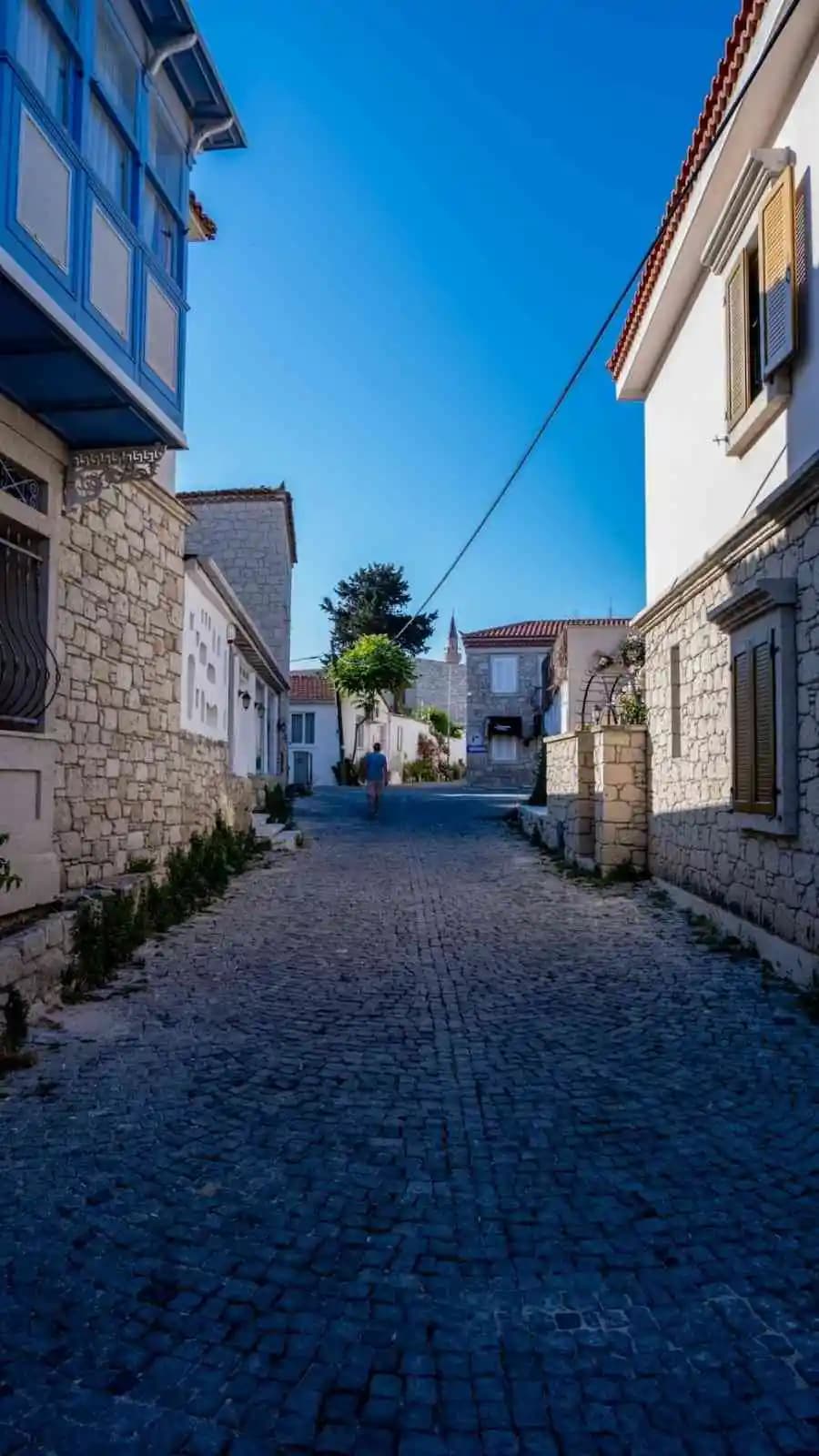 A cobbled lane between whitewashed stone houses with wooden shutters, under a clear blue sky