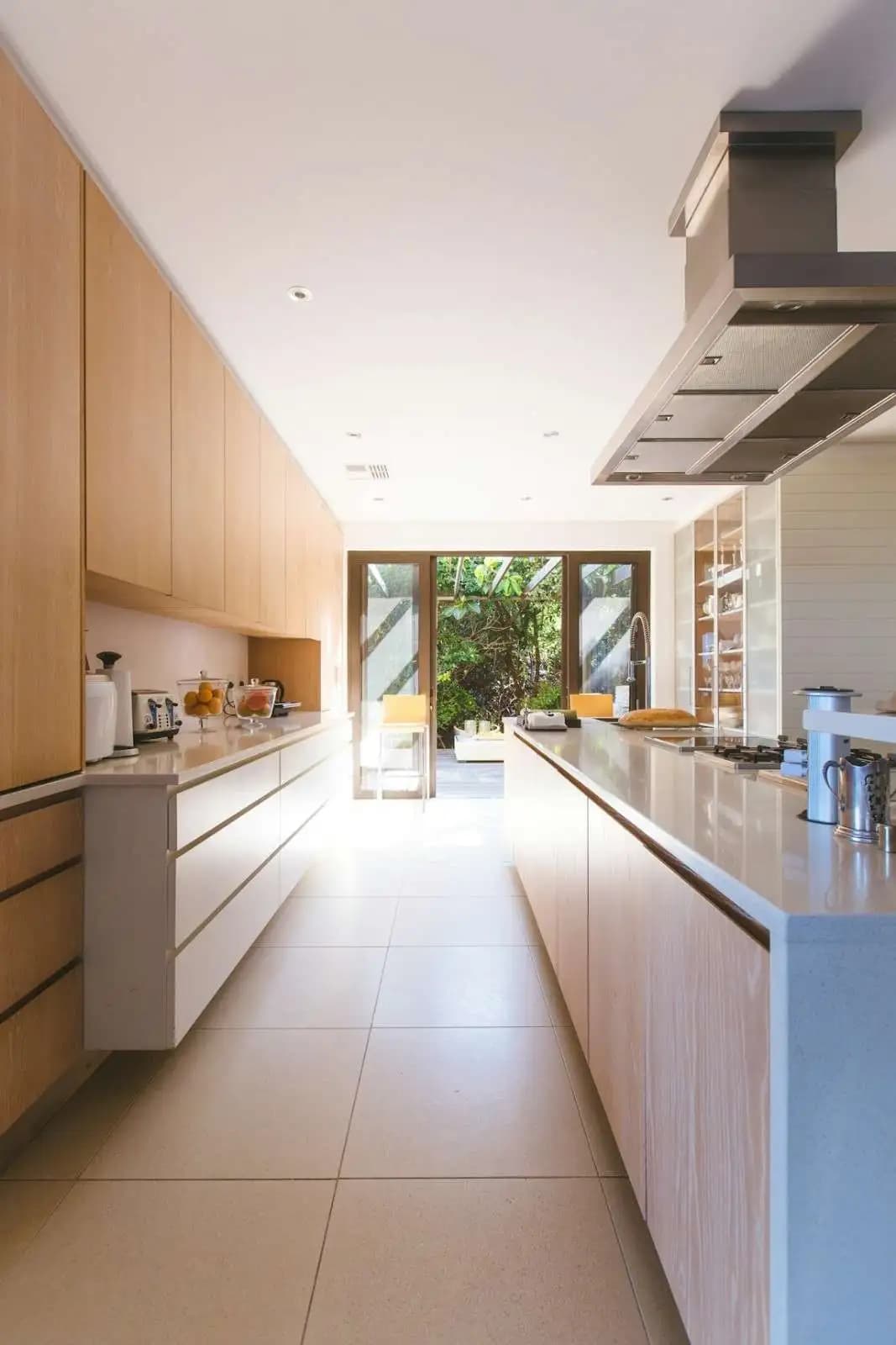 A bright home kitchen with timber cupboards, opening onto a leafy garden