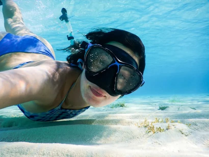 A snorkeler in a mask gliding over a sandy sea floor