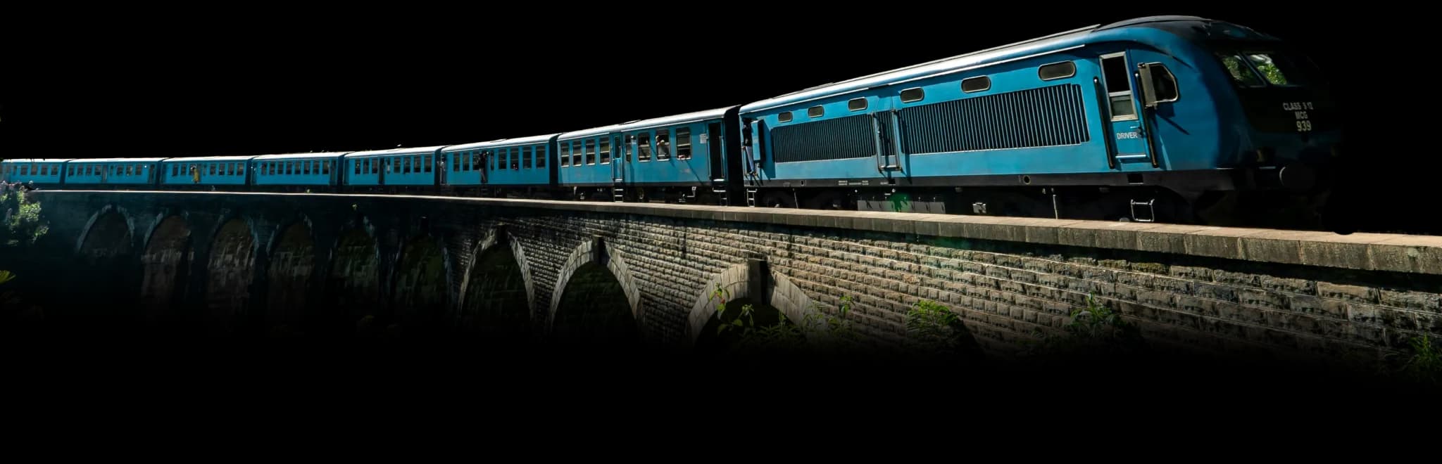 Blue Sri Lankan passenger train crossing a historic stone arch bridge in the hill country