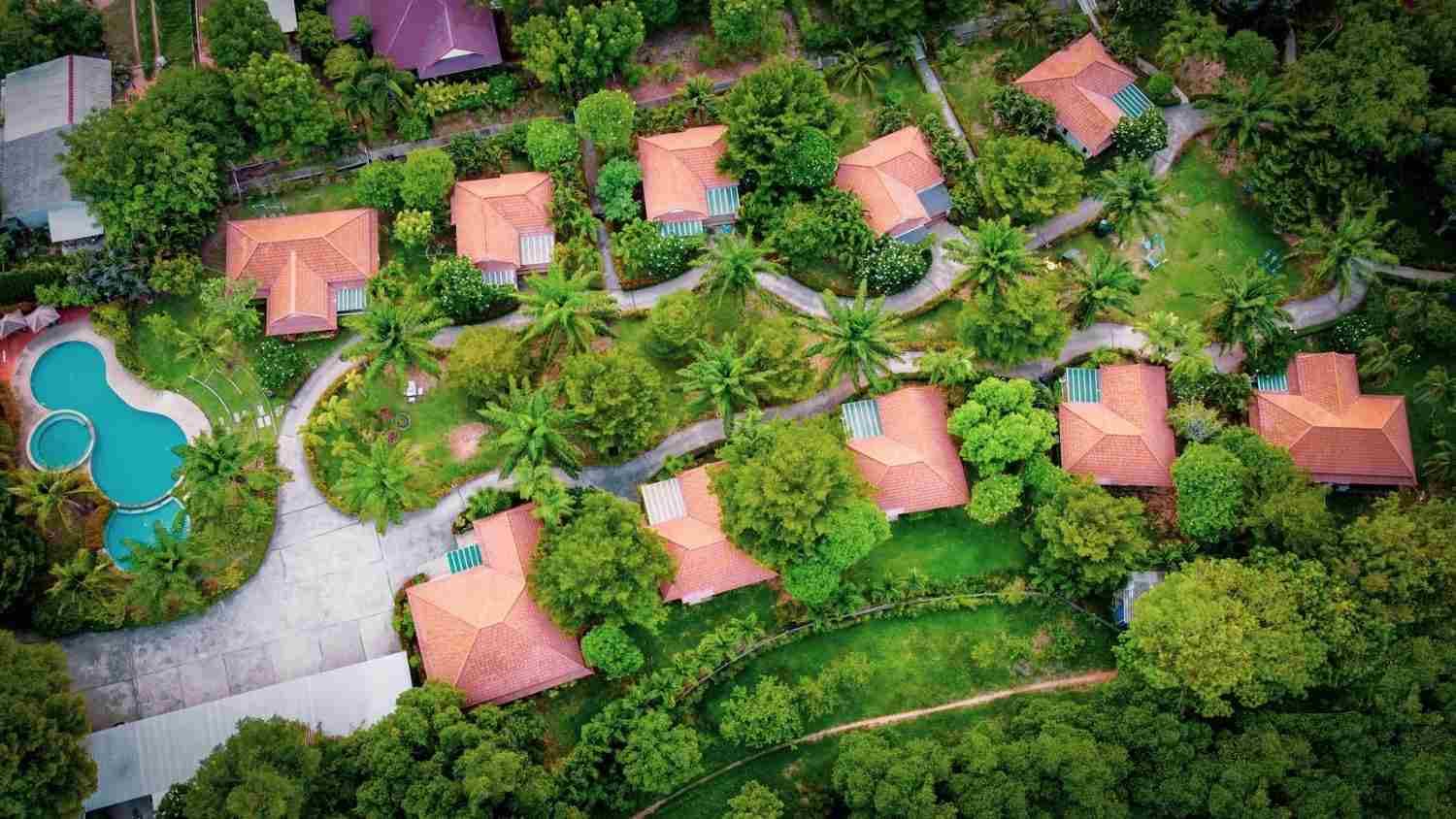 Red-roofed villas among palms and lawns around a curving pool, seen from above