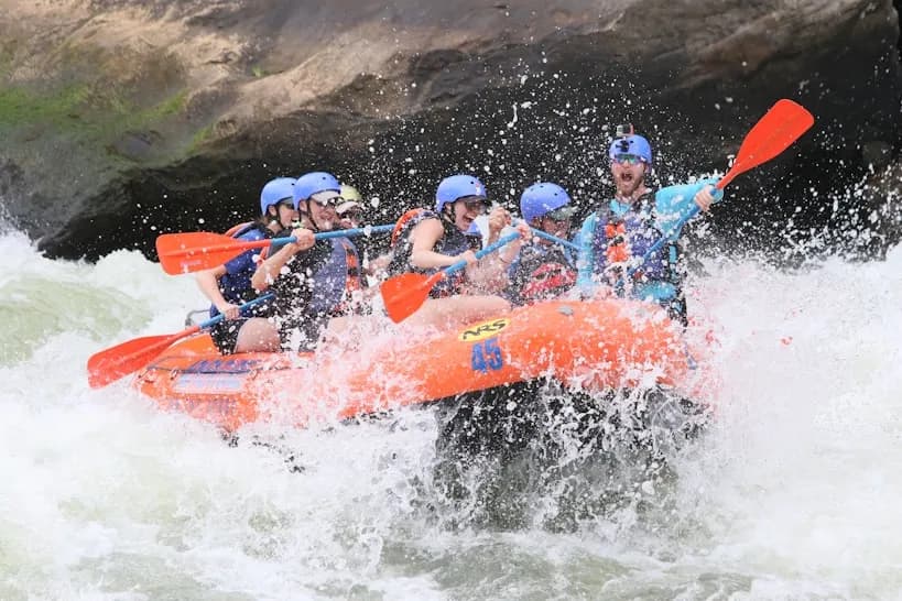 A team paddling an orange raft through white water