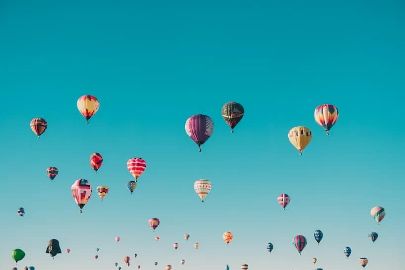 Dozens of hot air balloons rising into a clear blue sky