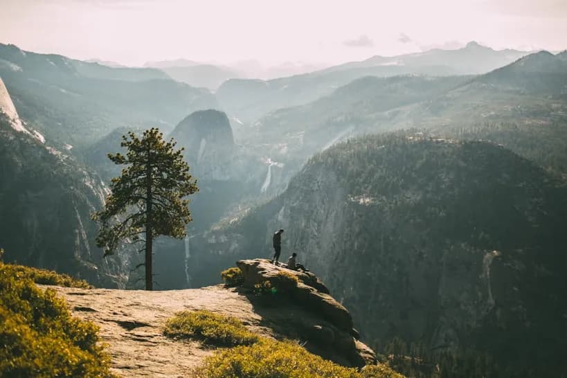 Two hikers on a rocky outcrop above a forested valley and distant waterfalls